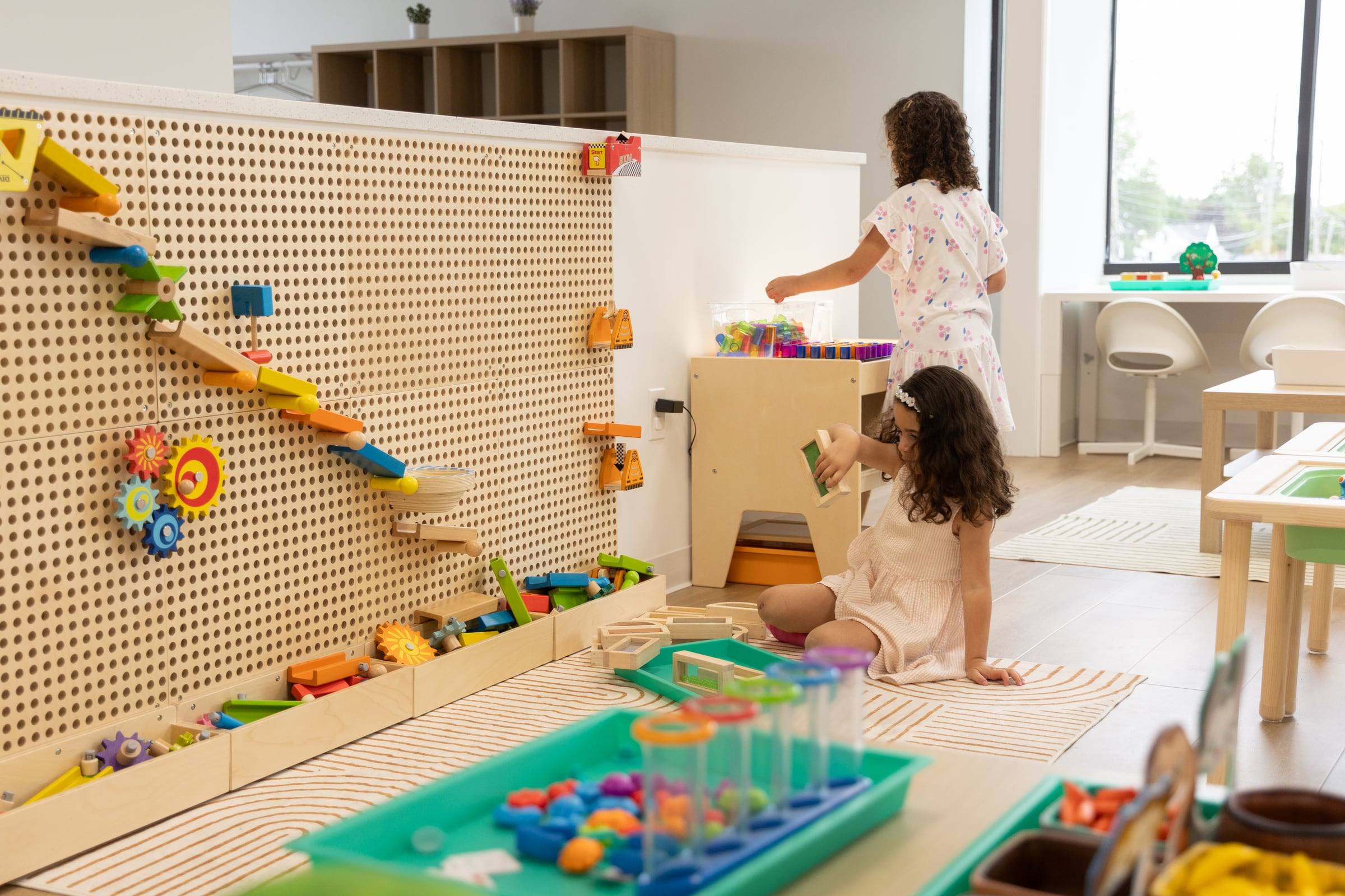 Two girls building a marble run on the peg wall